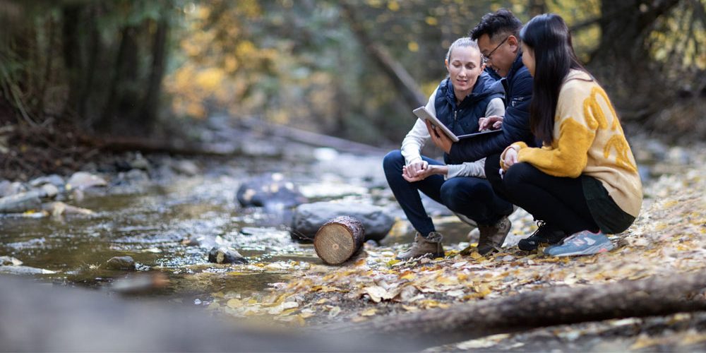 People crouching on the ground next to a river