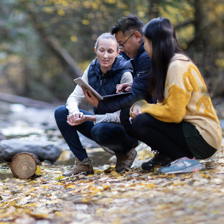 People crouching on the ground next to a river